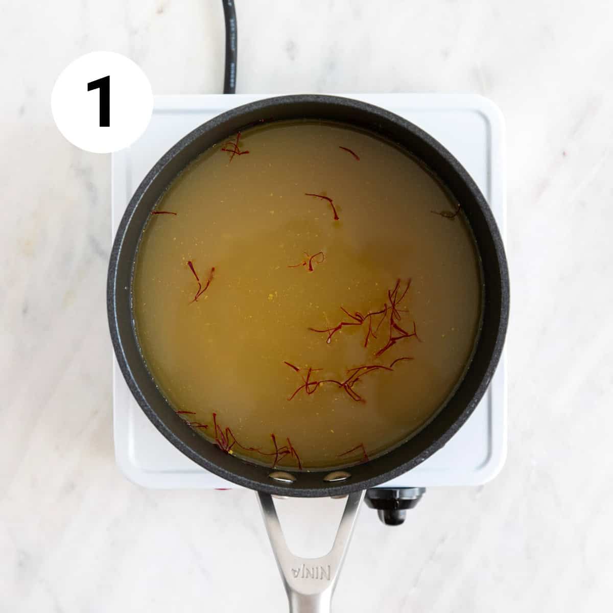 Vegetable broth and saffron threads in a saucepan.