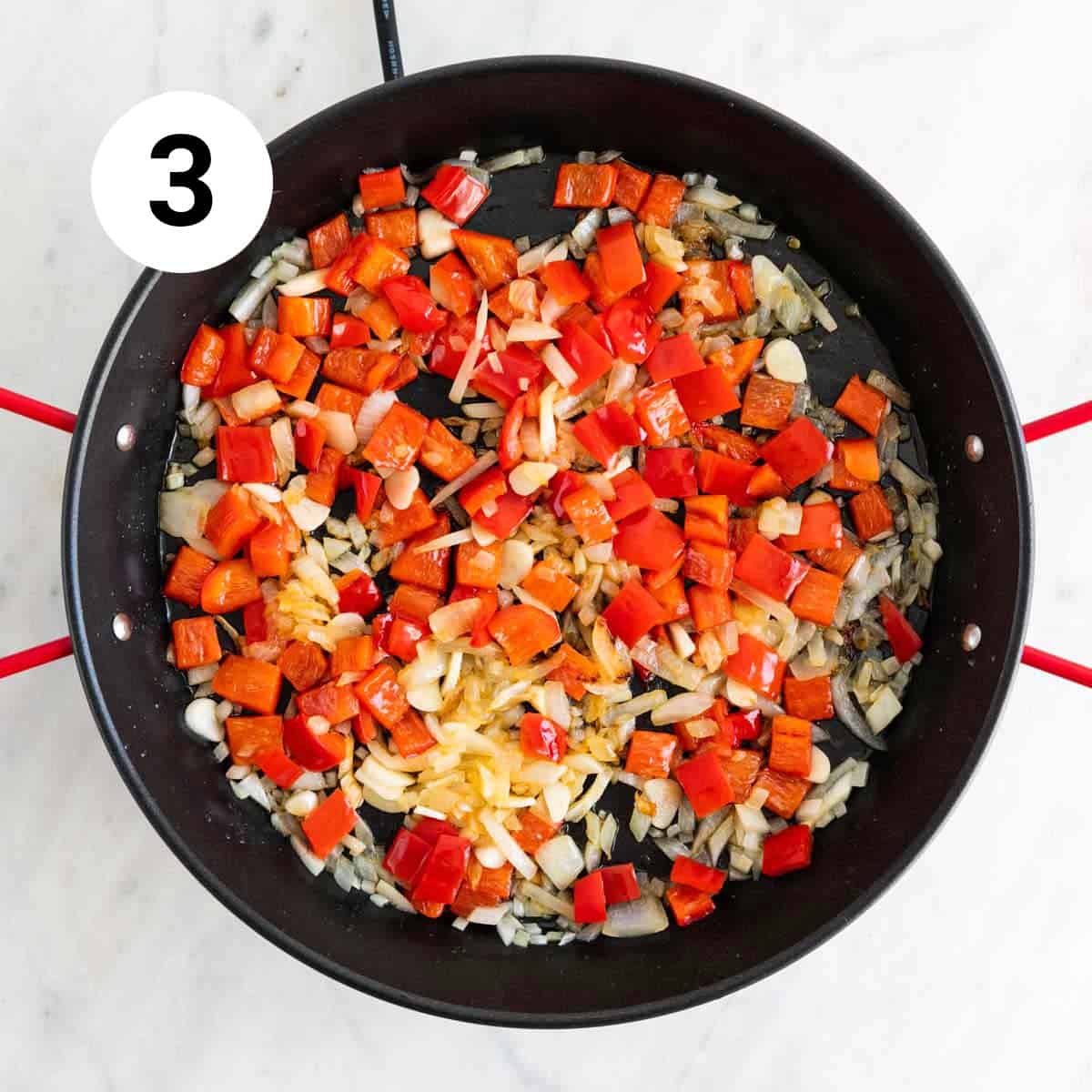Onion, red bell pepper, and garlic sautéed in a paella pan.