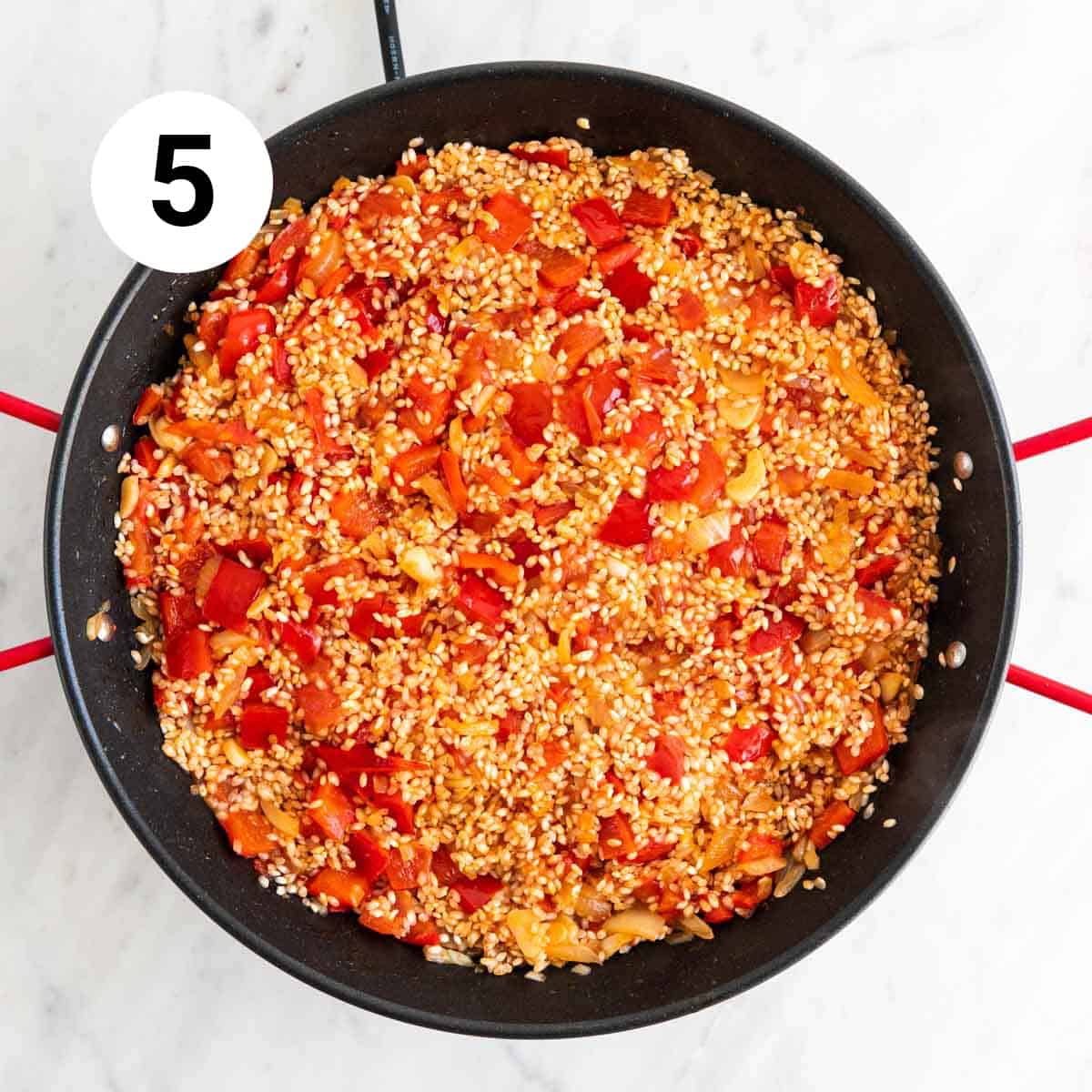 Sautéed vegetables and rice in a paella pan.