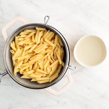 Cooked pasta in a pot and reserved pasta water in a bowl.