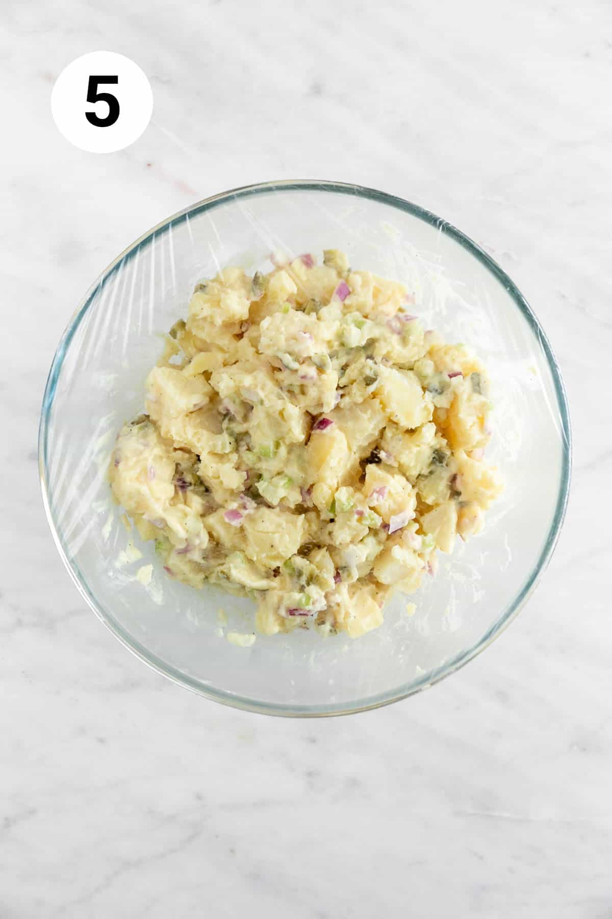 Bowl of vegan potato salad covered with plastic wrap.