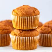Stacked vegan pumpkin muffins with more muffins in the background.