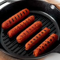 Square photo of some vegan sausages on a skillet