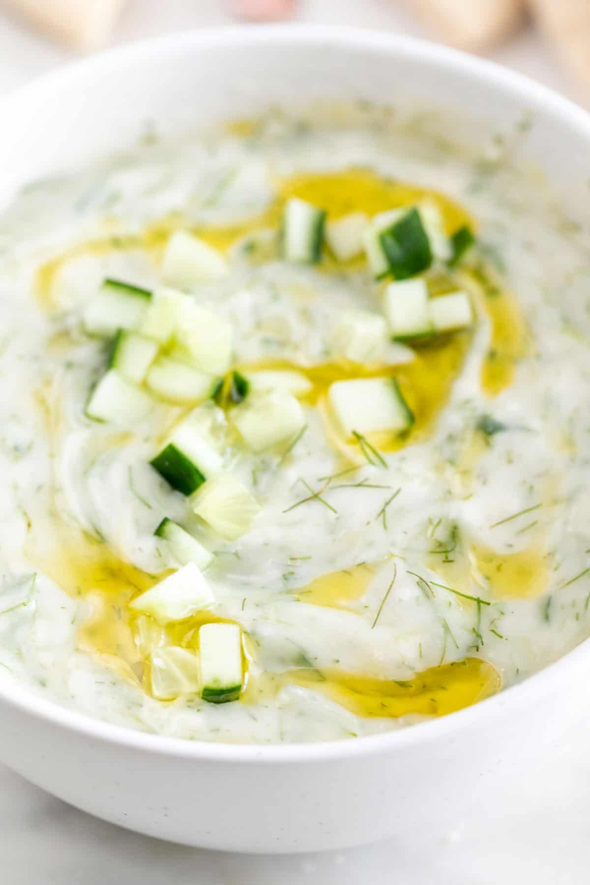Garnished vegan tzatziki sauce bowl with cucumber and olive oil.