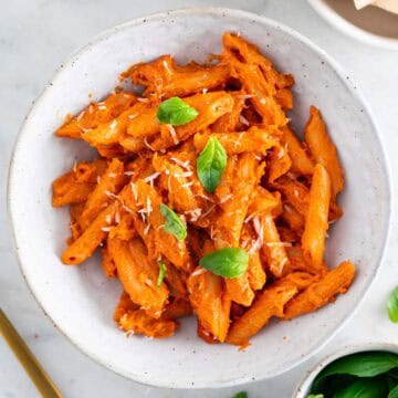 Vegan penne alla vodka in a bowl, garnished with basil and vegan parmesan cheese.