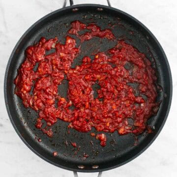Sautéed onion and garlic with tomato paste, salt, and pepper in a skillet.