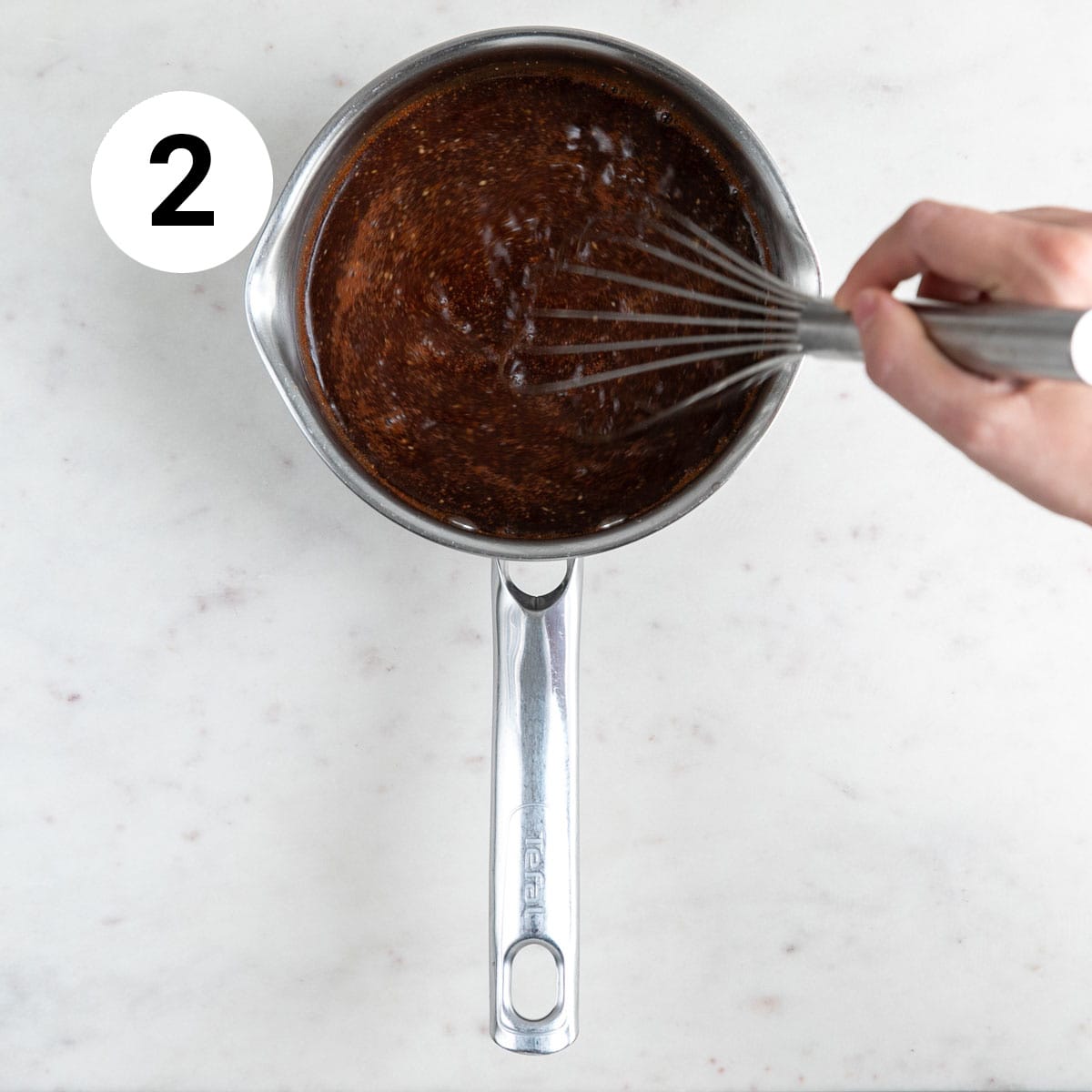 Hand whisking sauce in saucepan.