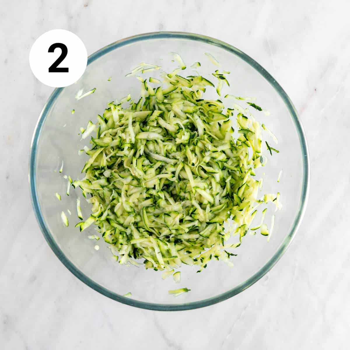 Grated zucchini with salt in a bowl after releasing moisture.