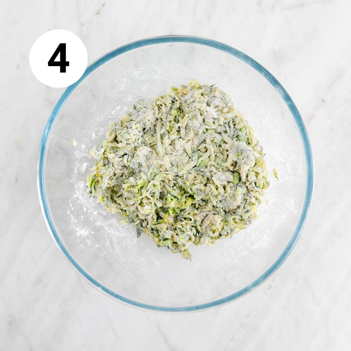 Zucchini mixed with flour, baking powder, black pepper, and spring onions in a bowl.