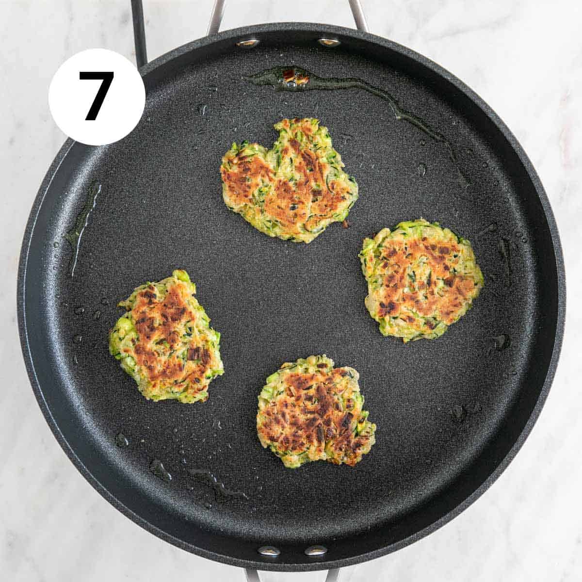 Vegan zucchini fritters fully cooked in a frying pan.