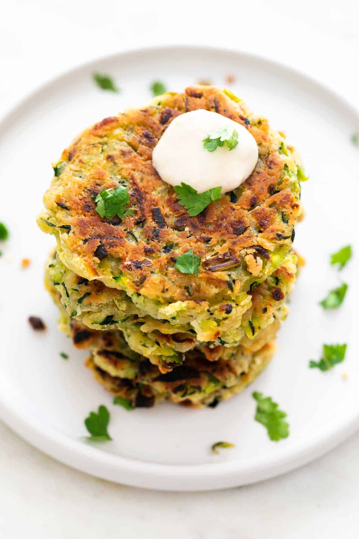 Vegan zucchini fritters served on a plate with a dollop of vegan sour cream and parsley.