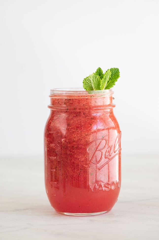 Side shot of a jar of watermelon smoothie decorated with mint leaves