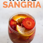 A picture of a glass with fresh fruit, ice cubes and white sangria with