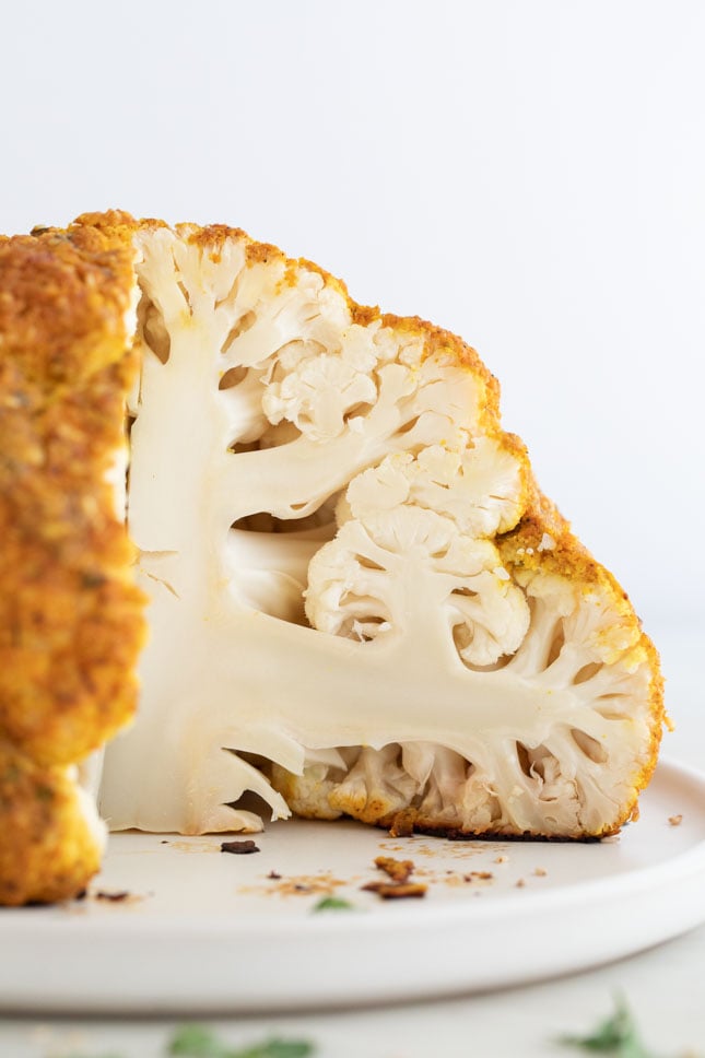 A side picture of a whole roasted cauliflower cut onto a plate 