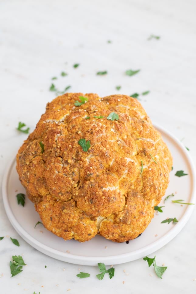 A shot of a head of cauliflower roasted onto a dish and garnished with some parsley
