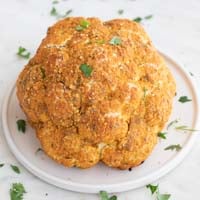 A small picture of a whole roasted cauliflower with some chopped parsley on top